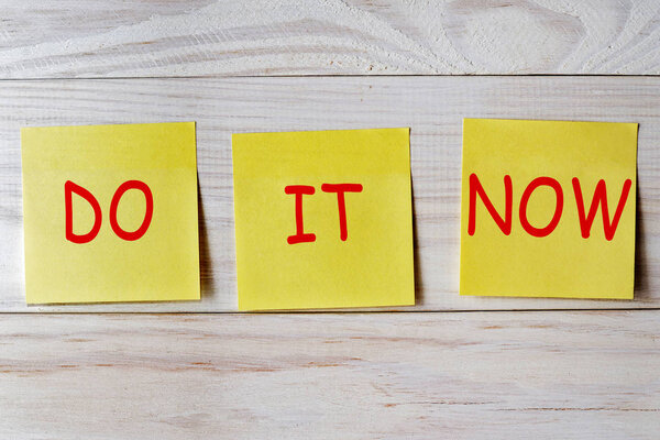 Do it now written on sticky note on wooden background