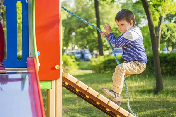 Маленький хлопчик піднімається на дитячий пагорб, що тримає мотузку. Дитина грає на дитячому майданчику — стокове фото