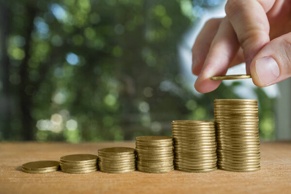 Male's hand put coin stack on money staircase. Business growing and saving money concept