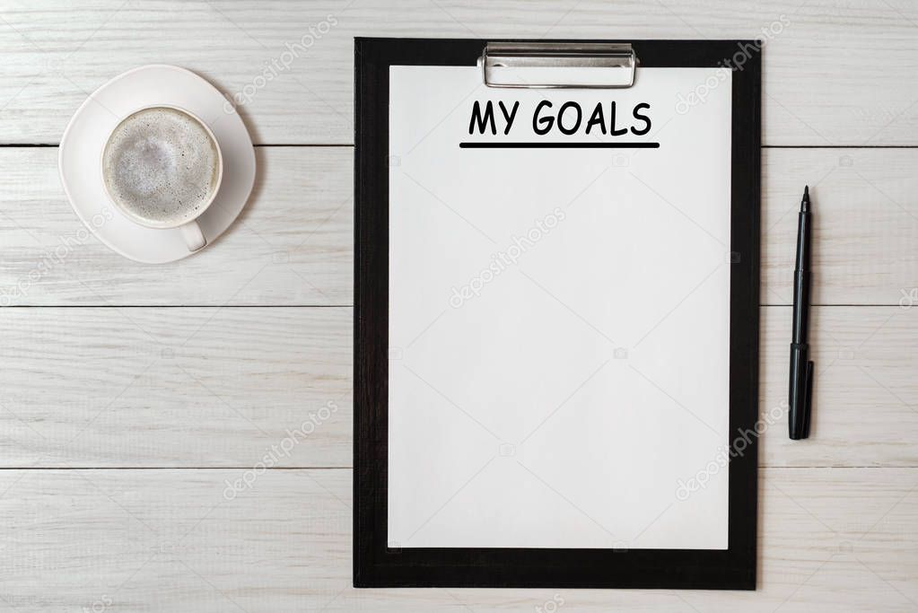 My goals list on note pad paper with pen and coffee on wooden table