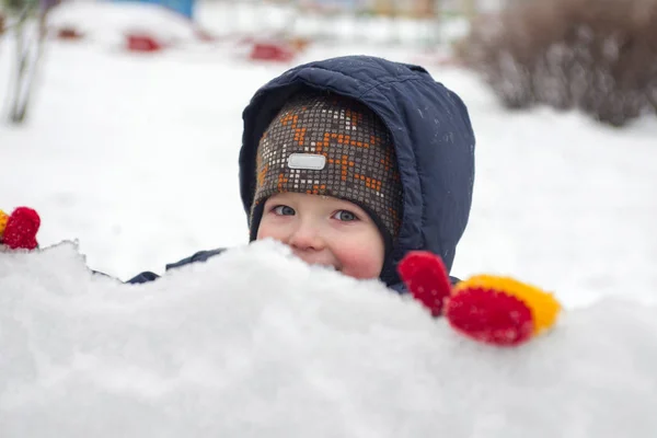 Ett litet barn ser ut ur snö eller isbitar. Ett barn leker med snö — Stockfoto
