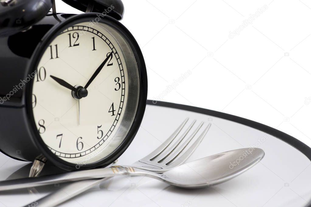 Black alarm clock with fork and knife on the plate. Isolated on white. Time to eat. Weight loss or diet concept