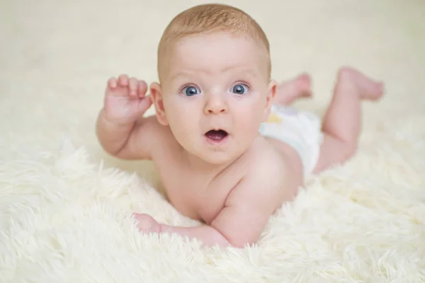 Alegre bebé lindo bajo una manta blanca mirando algo. Niño recién nacido que se relaja en la cama después del baño o ducha. Concepto de cuidado infantil y del bebé — Foto de Stock