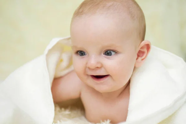 Alegre bebé lindo bajo una manta blanca mirando algo. Niño recién nacido que se relaja en la cama después del baño o ducha. Concepto de cuidado infantil y del bebé — Foto de Stock