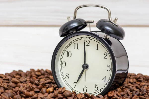 Väckarklocka och kaffebönor på en vit trä bakgrund. En väckarklocka som står på kaffebönorna. Kaffetidskoncept — Stockfoto