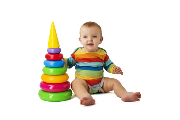 Okouzlující roztomilé dítě v montérkách hraje s barevnou plastovou pyramidou sedí na bílém pozadí. Dítě sbírá barevnou pyramidu — Stock fotografie