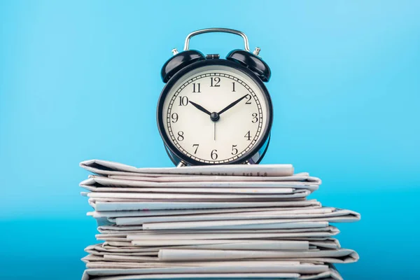 Newspapers and clock on blue background. Alarm clock and newspapers on table near color wall — 스톡 사진