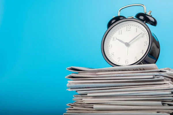 Newspapers and clock on blue background. Alarm clock and newspapers on table near color wall — 스톡 사진