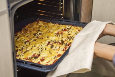 Kadın ev hanımı evde fırınla pizza pişiriyor.