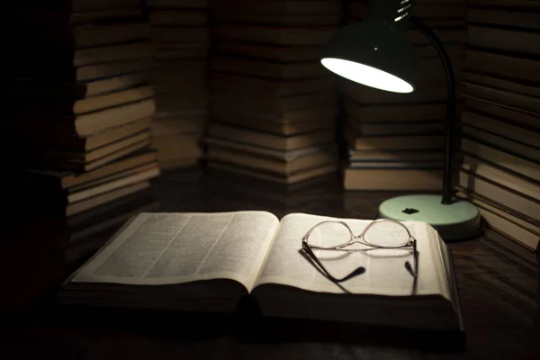 La lampe et le livre sur la table. Lire un livre avec l'éclairage de la lampe dans le noir. Livres sur table en bois sous lampe — Photo