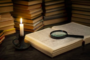 Mumların altında eski kitap ve büyüteç var. Mum ışığında, ahşap bir masanın üzerinde eski bir kitap. Eğitim kavramı