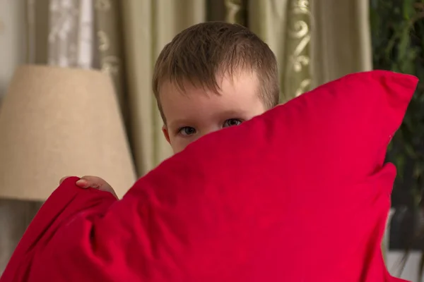 Dítě vykoukne zpoza polštáře. Chlapec se schovává za polštářem. — Stock fotografie