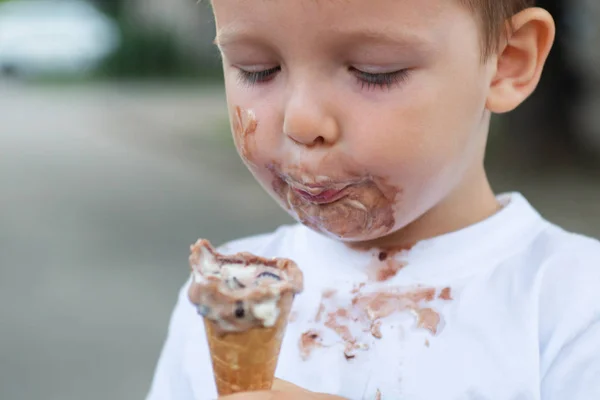 Счастливый ребенок ест мороженое. Мальчик с грязным лицом ест мороженое — стоковое фото
