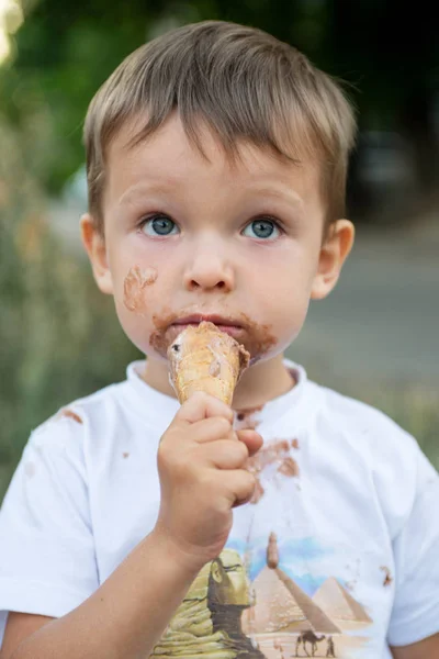 Счастливый ребенок ест мороженое. Мальчик с грязным лицом ест мороженое — стоковое фото