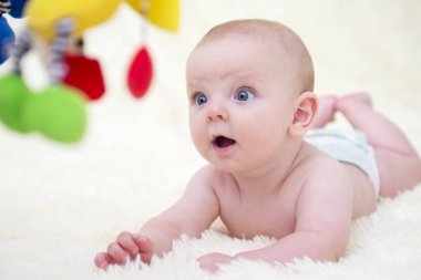 Küçük bir çocuk karnının üstüne yatar ve oyuncaklara bakar. Küçük bebek evinde, yatağında oyuncaklarla oynuyor. Çocukluk ya da bebek bakımı kavramı.