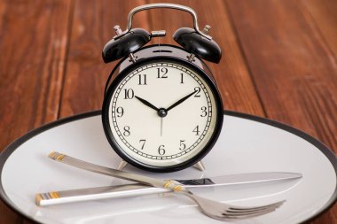 Çalar saat tabakta bıçak ve çatalla ahşap zemin üzerinde. Yemek zamanı. Kilo kaybı veya diyet kavramı.