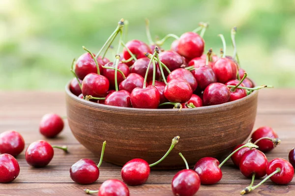 Ripe sweet cherries in ceramic bowl on a wooden table on natural background. Sweet cherries in garden.