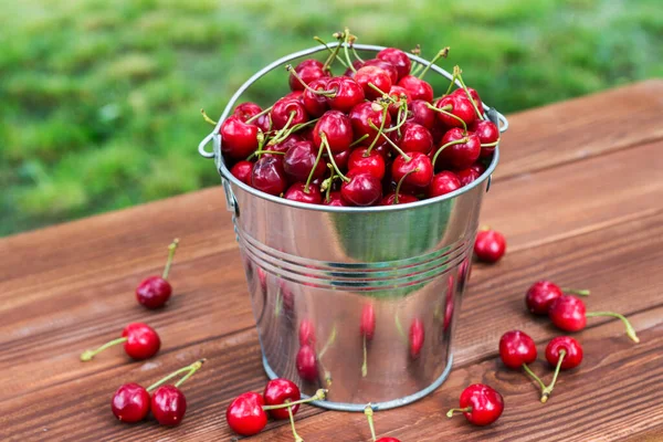 Tahta arka plandaki kovada taze kırmızı kiraz. Tahta arka planda metal kovada olgun kırmızı kirazlar..