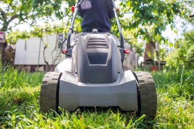 Adam çimleri biçiyor. Çim biçme makinesi olan adam bahçede yeşil çim biçiyor. Bahçıvanlık.