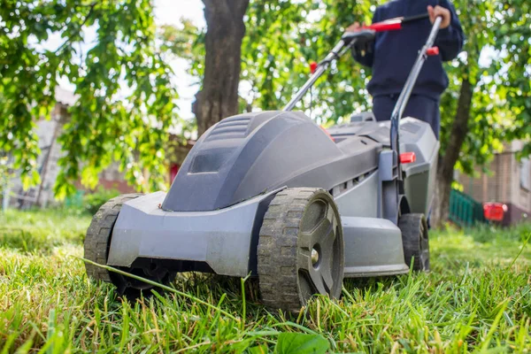 Adam çimleri biçiyor. Çim biçme makinesi olan adam bahçede yeşil çim biçiyor. Bahçıvanlık.