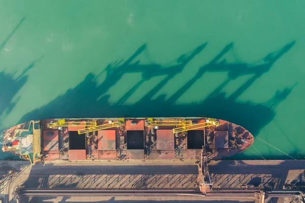 Limandaki bir kömür terminalinin rıhtımında büyük bir taşıyıcı duruyor. Kargo açık bir depodan nakliye bandı ve makine yüklü bir gemiye yükleniyor.