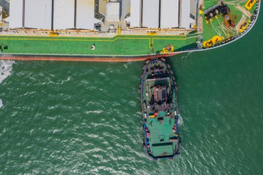 Bir römorkör bir kargo gemisini iskeleye itiyor. Yukarıdan görüntüle