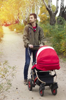 Genç baba anne yardımcı olur, nehir kıyısında bir bebek arabası park ile yürüyor