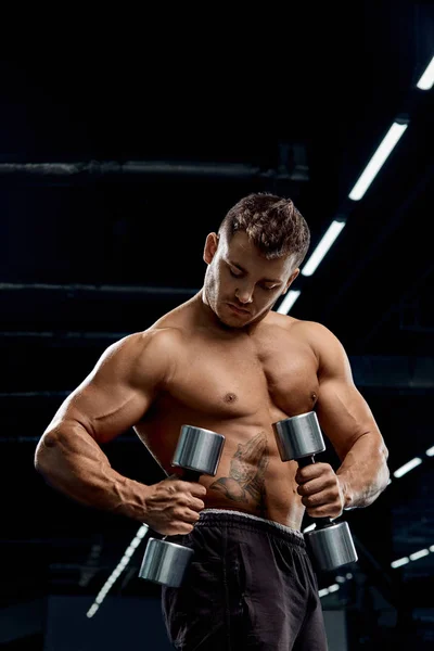 Muscular bodybuilder doing exercises with dumbbell in gym.Strong