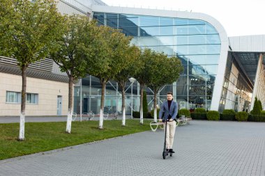 Gün batımında havaalanının yanındaki yolda e-scooter kullanan genç yakışıklı bir adam. Modern elektrikli scooter 'la son moda şehir ulaşımı. Çevre dostu hareketlilik kavramı.