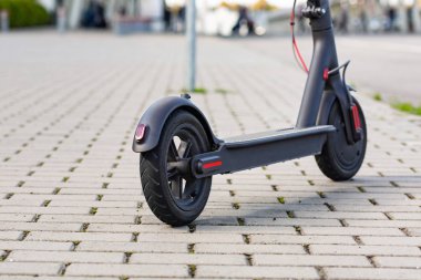 Gün batımında şehir manzarasında kaldırıma park edilmiş e-scooter 'ın yakın görüntüsü. Modern elektrikli scooter 'la son moda şehir ulaşımı. Çevre dostu hareketlilik kavramı.