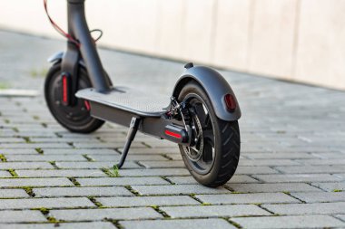 Gün batımında şehir manzarasında kaldırıma park edilmiş e-scooter 'ın yakın görüntüsü. Modern elektrikli scooter 'la son moda şehir ulaşımı. Çevre dostu hareketlilik kavramı.