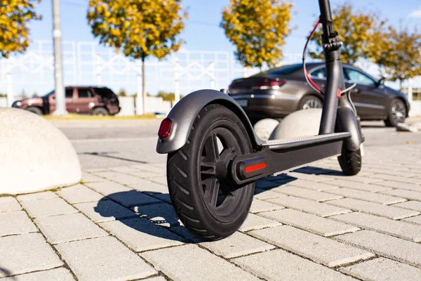 Gün batımında şehir manzarasında kaldırıma park edilmiş e-scooter 'ın yakın görüntüsü. Modern elektrikli scooter 'la son moda şehir ulaşımı. Çevre dostu hareketlilik kavramı.
