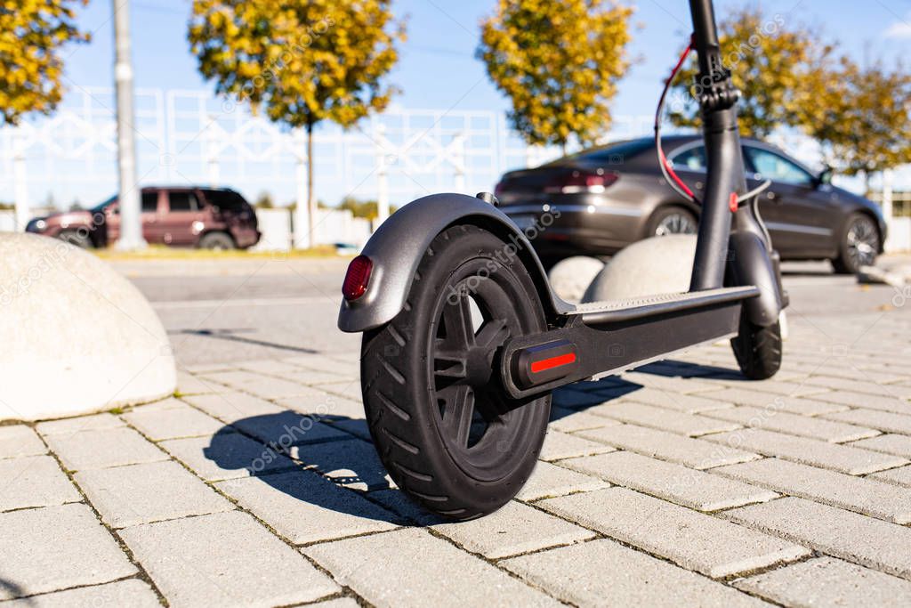 Close up view of e-scooter parked on sidewalk at cityscape on the sunset. Trendy urban transportation on modern electric scooter. Eco friendly mobility concept.