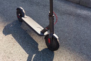 Gün batımında şehir manzarasında kaldırıma park edilmiş e-scooter 'ın yakın görüntüsü. Modern elektrikli scooter 'la son moda şehir ulaşımı. Çevre dostu hareketlilik kavramı.