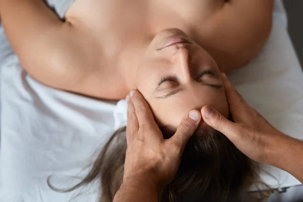 Joven hermosa mujer disfrutando de anti-envejecimiento masaje.Male facial terapeuta haciendo masaje de cabeza a la client.Professional femenina masseur.Relaxation, belleza, spa, cuerpo y rostro concepto de tratamiento — Foto de Stock