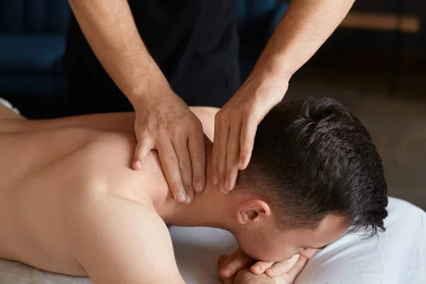 Νεαρός απολαμβάνει την πλάτη και shouders μασάζ σε spa.Professional θεραπευτής μασάζ είναι η θεραπεία ενός ανδρικού ασθενή σε χώρα.Χαλάρωση, την ομορφιά, το σώμα και το πρόσωπο έννοια θεραπείας.Home μασάζ — Φωτογραφία Αρχείου