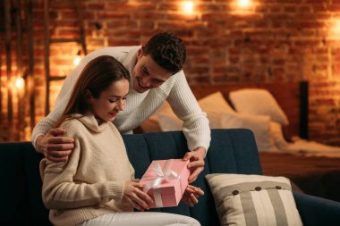 Yakışıklı bir adam güzel kız arkadaşına hediye sunuyor ve gülümsüyor. Güzel genç bir çift birlikte vakit geçirmekten zevk alıyor. Sevgililer Günü, ilişkiler ve insanlar konsepti.