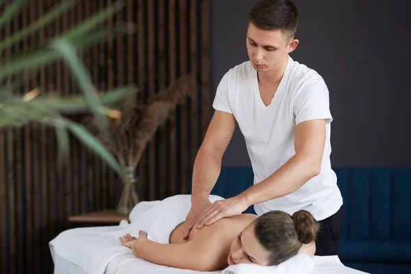 Ung vacker kvinna njuter av rygg och shouders massage i spa.Professionell massage terapeut behandlar en kvinnlig patient i lägenhet.Avkoppling, skönhet, kropp och ansikte behandlingskoncept.Hem massage — Stockfoto
