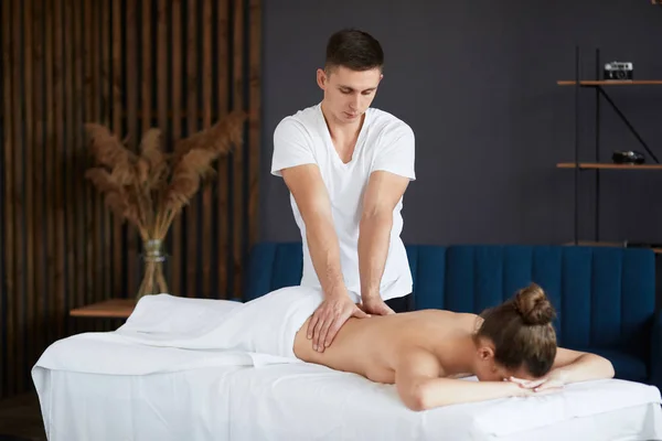 Młoda piękna kobieta korzystających z pleców i krzyczy masaż w spa.Professional masażysta leczy pacjentkę w apartamencie.Relaks, piękno, ciało i leczenie twarzy koncept.Home masaż — Zdjęcie stockowe