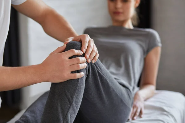 Kvinnelig pasient som gjør fysisk trening med fysioterapeut. Mannlig terapeut som behandler skadet kne hos unge idrettsutøvere. Post traumatisk rehabilitering, sportsfysioterapi, rekonvalesenskonsept – stockfoto