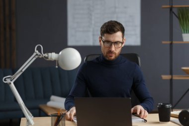 Ofiste dizüstü bilgisayarla çalışan bir mimar. İş yerinde oturan gözlüklü yakışıklı sakallı adamın iş portresi. Kendinden emin iş adamı başarılı oldu. İş konsepti
