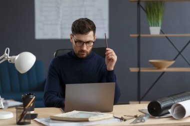 Ofiste dizüstü bilgisayarla çalışan bir mimar. Mühendis mimari plan üzerinde düşünüyor, inşaat projesi için yeni fikirler arıyor. İş yerinde oturan yakışıklı sakallı adamın portresi. İş konsepti