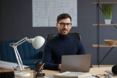 Ofiste dizüstü bilgisayarla çalışan bir mimar. İş yerinde oturan gözlüklü yakışıklı sakallı adamın iş portresi. Kendinden emin iş adamı başarılı oldu. İş konsepti
