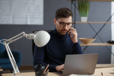 Ofiste telefonla konuşan bir mimar. Güvenilir iş adamları iş ortaklarıyla pazarlık eder. İş yerinde oturan gözlüklü yakışıklı sakallı adamın iş portresi. İş konsepti