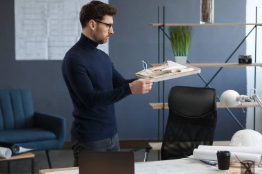 Ofiste çalışan mimar 3D model bir bina. Mühendis bina planını inceliyor, inşaat projesi için yeni fikirler arıyor. İş yerindeki yakışıklı sakallı adam. İş inşa kavramı
