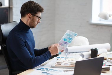 Ofiste renk paletiyle çalışan bir mimar. Mühendis renk örnekleri kullanarak bina için renkler seçiyor, inşaat projesi için yeni fikirler arıyor. İş yerinde sakallı yakışıklı bir adamın portresi.