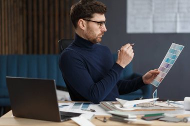 Ofiste renk paletiyle çalışan bir mimar. Mühendis renk örnekleri kullanarak bina için renkler seçiyor, inşaat projesi için yeni fikirler arıyor. İş yerinde sakallı yakışıklı bir adamın portresi.
