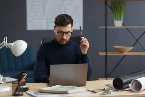 Architecte travaillant au bureau avec ordinateur portable.Ingénieur réfléchit sur le plan architectural, la recherche de nouvelles idées pour le projet de construction. Portrait d'un bel homme barbu assis sur le lieu de travail. Concept d'entreprise — Photo