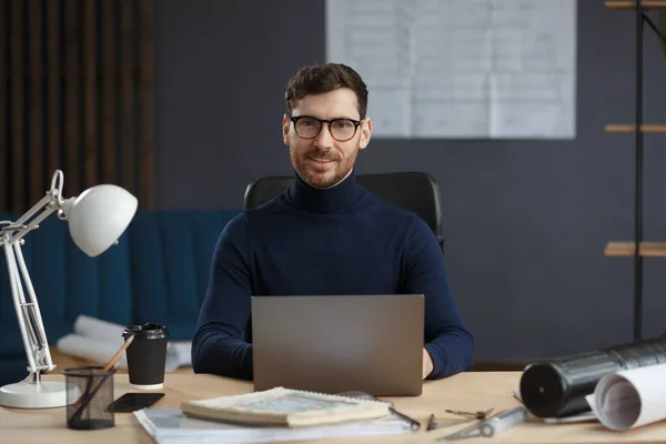 Egy építész, aki laptoppal dolgozik. Üzleti portré egy jóképű szakállas férfiról, aki szemüvegben ül a munkahelyén. A magabiztos üzletember sikeres lett. Üzleti koncepció — Stock Fotó