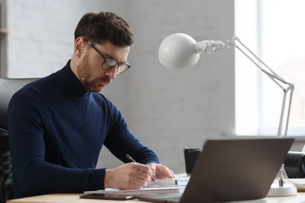 Architect werkt in kantoor met blauwdrukken. Ingenieur inspecteert architectonisch plan, schets een bouwproject.Portret van knappe bebaarde man zittend op het werk. Bedrijfsbouwconcept — Stockfoto